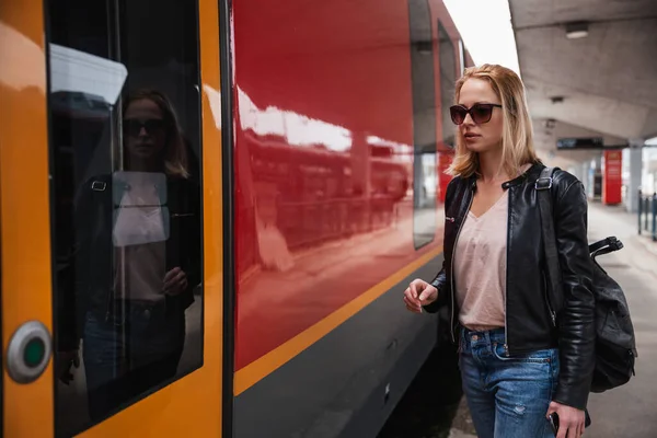 청바지와 셔츠와 자켓을 선글라스를 금발의 기차역 승강장에서 열차를 — 스톡 사진