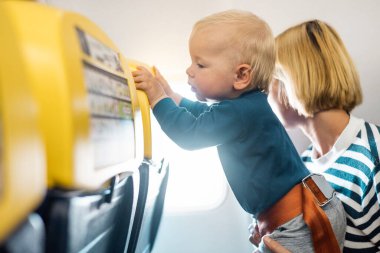 Anne ve bebek bebek çocuk ticari uçuşta uçuyor, uçakla seyahat ediyor, cam kenarında yan yana oturuyor. Çocuklarla uçmak