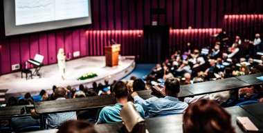 İş ve girişimcilik sempozyumu. İş toplantısında kadın konuşmacı bir konuşma yapıyor. Konferans salonunda dinleyiciler. İzleyicilerin tanınmayan katılımcılarının arka görünümü.