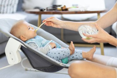 Anne, bebeğini bebek koltuğunda meyve püresiyle besliyor. Bebek katı gıda tanıtım konsepti