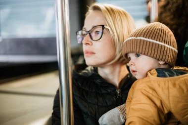 Anne ayakta dururken ve otobüsü tutarken çocuğunu taşıyor. Anne, toplu taşıma aracında giderken bebeğini kollarında tutuyor. Küçük tatlı çocuk annesiyle seyahat ediyor.