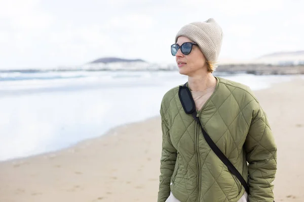 春天长沙沙滩上穿着绿色棉衣 羊毛帽和太阳镜的年轻时尚女子的画像 — 图库照片