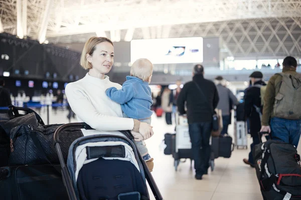 幼い男の子の子供と一緒に旅行しているお母さん 歩くこと 空港ターミナル駅でベビーベビーカーと手荷物カートを押してください 子供のコンセプトで旅行 — ストック写真