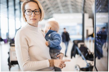 Anne çocuğuyla seyahat ediyor, bebeğini havaalanı terminalinde tutuyor uçuş saatlerini kontrol ediyor, uçağa binmeyi bekliyor. Çocuk konseptiyle seyahat