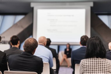 İş ve girişimcilik sempozyumu. İş toplantısında kadın konuşmacı bir konuşma yapıyor. Konferans salonunda dinleyiciler. İzleyicilerin tanınmayan katılımcılarının arka görünümü.