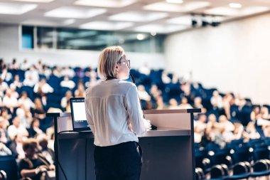 Kadın konuşmacı şirket iş konferansı hakkında bir konuşma yapıyor. Konferans salonundaki tanınmayan insanlar. İş ve Girişimcilik etkinliği