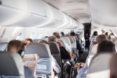 Uçakta koltuklarda yolcular ve koridorda yürüyen, insanlara hizmet eden üniformalı hostesler var. Ticari ekonomi uçuş hizmeti kavramı