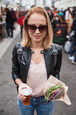 Lezzetli organik somonlu vejetaryen burger ve açık hava birası üzerine ev yapımı IPA birası tutan genç bir kadın Ljubljana, Slovenya 'da bir burger sokak yemeği festivali.