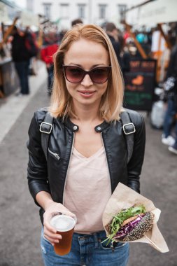 Lezzetli organik somonlu vejetaryen burger ve açık hava birası üzerine ev yapımı IPA birası tutan genç bir kadın Ljubljana, Slovenya 'da bir burger sokak yemeği festivali.