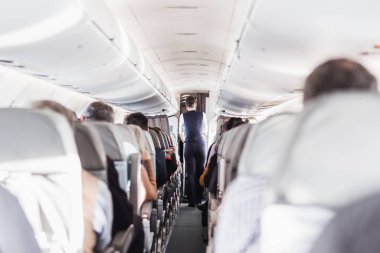 Uçakta koltuklarda yolcular ve koridorda yürüyen, insanlara hizmet eden üniformalı hostesler var. Ticari ekonomi uçuş hizmeti kavramı