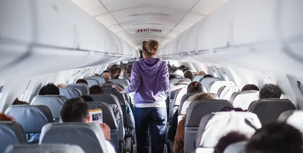 stock image Interior of airplane with passengers on seats and female traveler walking the aisle. Commercial economy flight service concept