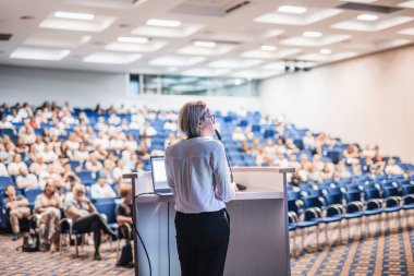 Kadın konuşmacı şirket iş konferansı hakkında bir konuşma yapıyor. Konferans salonundaki tanınmayan insanlar. İş ve Girişimcilik etkinliği