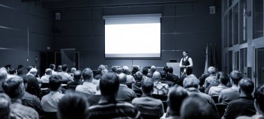 Sözcü İş Toplantısı 'nda konuşma yapacak. Konferans salonunda dinleyiciler. İş ve Girişimcilik konsepti. Siyah-beyaz mavi tonlu görüntü.