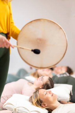 Tibet davuluyla grup terapisi. Etrafı bakır kaselerle çevrili bir grup kadın için ahşap zeminde yatıyorlar. Meditasyon ve rahatlama
