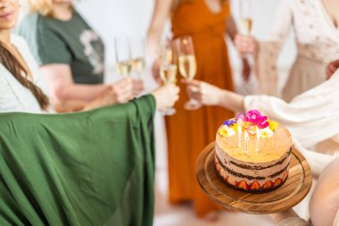 Doğum günü sürpriz partisi. Bir grup neşeli bayan arkadaş kişisel başarı hikayelerini kutluyorlar. Şampanyayla kadeh kaldıran gülümseyen kızlar. Biri elinde mumlarla doğum günü pastası tutan kızlar..