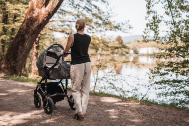 Slovenya 'nın Ljubljana kentindeki Koseski Bajer şehir parkında sıradan giyinmiş bir annenin bebek arabasıyla dolaşması. Aile, çocuk ve ebeveynlik kavramı.