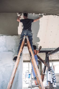 İş yerindeki erkek müteahhit, inşaat malası kullanarak eski duvarı sıvayıp restore ediyor..