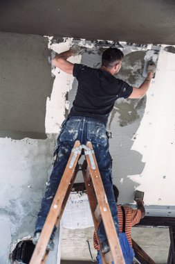 İş yerindeki erkek müteahhit, inşaat malası kullanarak eski duvarı sıvayıp restore ediyor..