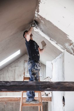 İş yerindeki erkek müteahhit, inşaat malası kullanarak eski duvarı sıvayıp restore ediyor..