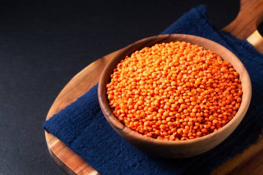 Healthy food concept red lentils in wooden bowl on black background with copy space