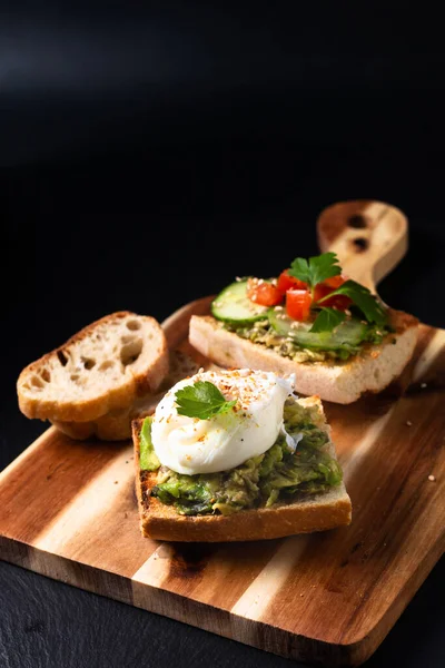 Healthy food concept poached egg and avocado toast on wooden board on black slate stone background
