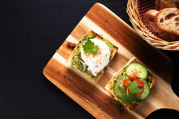 Healthy food concept poached egg and avocado toast on wooden board on black slate stone background