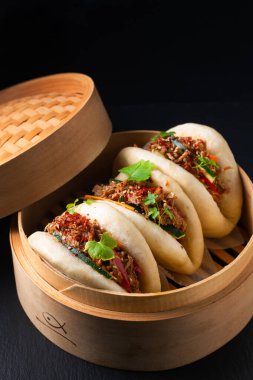 Food concept Homemade organic Pulled Beef Bao Buns or Gua Bao in bamboo stream tray on black background with copy space