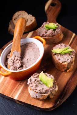 Food concept Chicken Liver spread Pate Baguette bite on wooden board on black background with copy space
