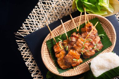 Tayland sokak yemekleri konsepti Moo ping, Mu Ping, Tayland usulü ızgara bbq domuz şişleri ve siyah arka planda pirinç çubuğu ve fotokopi alanı.