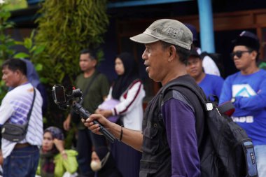 Tarakan, Endonezya 7 Ekim 2023: Bir erkek içerik yaratıcısı kalabalığın içinde akıllı telefon kamerasıyla içerik yaratıyor                               