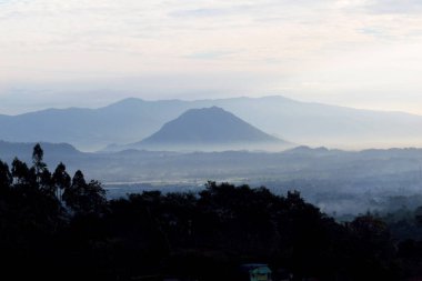 Serene misty valley unfolds at dawn, offering a breathtaking mountain panorama with tranquil, atmospheric beauty.