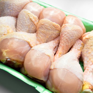 Taze pişmemiş tavuk budu parçaları, yeşil pakette pişmeye hazır bebek, beyaz arka planda.