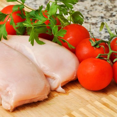 Taze çiğ tavuk eti göğüs parçaları, pişirmeye hazır, domates ve maydanozlu.
