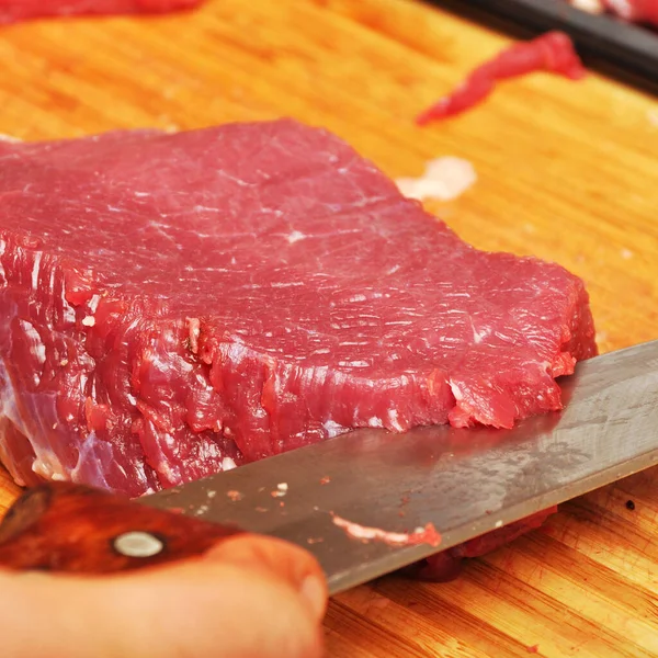 Clean very fresh red raw cow meat and a sharp knife, on cutting board