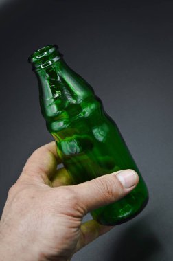 Gri arka planda izole edilmiş üç temiz yeşil boş soda şişesi ve el.