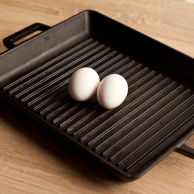 Siyah, iki organik beyaz yumurta içinde ağır demir ızgara tavası; modern meşe mutfak tezgahı, modern mutfak ekipmanları