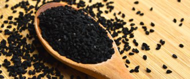 Tahta kaşıkta, bambu kesme tahtasının üzerinde bir sürü kuru siyah kimyon.