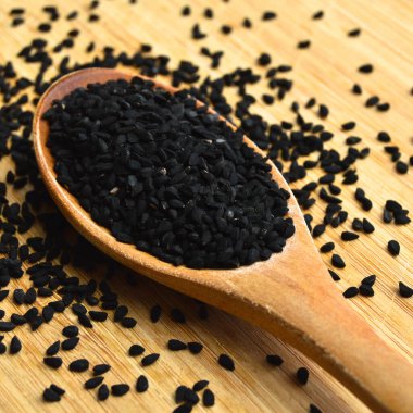 Tahta kaşıkta, bambu kesme tahtasının üzerinde bir sürü kuru siyah kimyon.