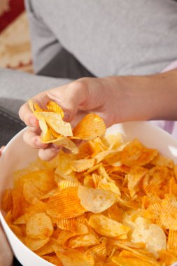 Pembe tişörtlü, elinde patates cipsi dolu beyaz tabak tutan ve yemeğe hazırlanan beyaz bir adam.