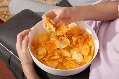 Pembe tişörtlü, elinde patates cipsi dolu beyaz tabak tutan ve yemeğe hazırlanan beyaz bir adam.