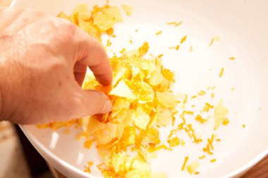Beyaz bir porselen tabakta patates cipsi var. Beyaz bir insan elinde patates cipsi tutuyor.