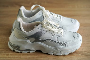 Yeni şık ve kullanışlı beyaz ayakkabılar, ahşap zeminde.