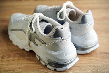 Yeni şık ve kullanışlı beyaz ayakkabılar, ahşap zeminde.