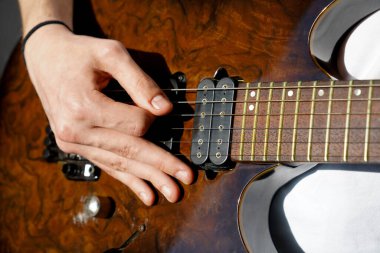Kafkasyalı bir müzisyenin elleri elektro gitar çalıyor, açık kahverengi renkli tahta gitar çalıyor.