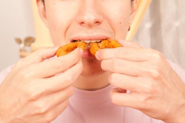 Beyaz bir adam elleriyle taze kızarmış soğan halkaları yiyor. Amerikan fast food kültürü.