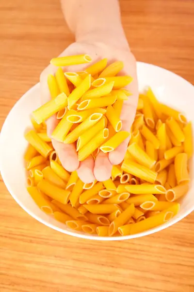 stock image Uncooked raw healthy and delicious pasta macaroni held by a Caucasian man in porcelain plate on wooden table