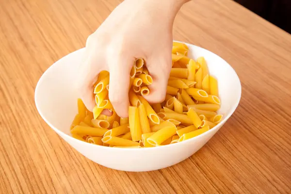 stock image Uncooked raw healthy and delicious pasta macaroni held by a Caucasian man in porcelain plate on wooden table