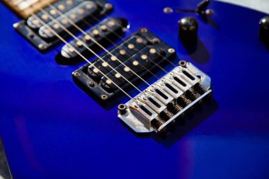 Elektro gitar köprüsü, teller ve pikap, ahşap boya mavisi, telli müzik aleti ile gitar pikapının detaylı görüntüsü.