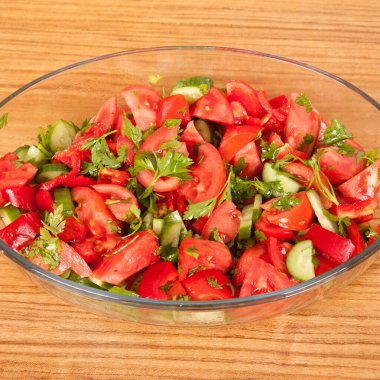 Lezzetli domateslerden, salatalıklardan, maydanozdan ve kırmızı biberden oluşan salata kahverengi ahşap bir masada cam bir tabakta.