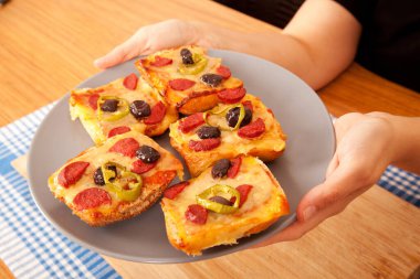 Beyaz tenli beyaz tenli, lezzetli ve lezzetli pizza parçalarını mavi peçete ve bambu kesme tahtasıyla gri tabakta tutuyor.